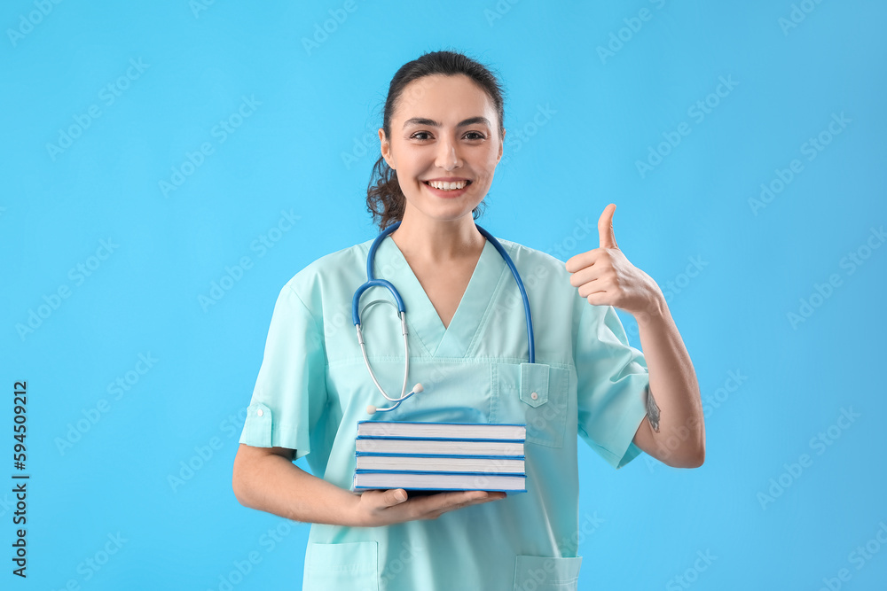 Female intern with books showing thumb-up on light blue background Female intern with books showing thumb-up on light blue background