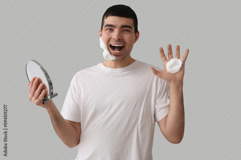 Funny young man applying shaving foam against light background Funny young man applying shaving foam against light background