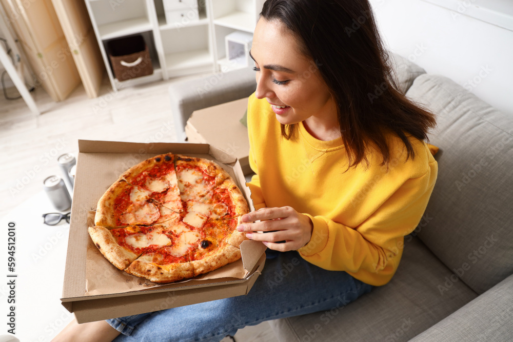Beautiful woman with box of tasty pizza sitting on sofa at home