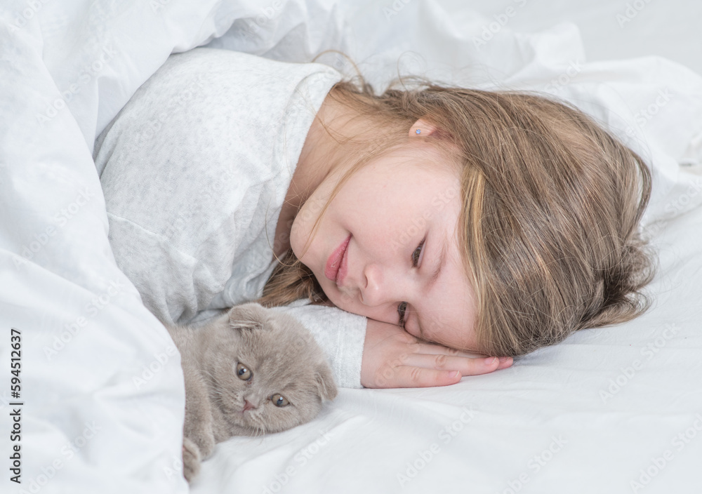 Smiling little girl and tiny kitten lying on the bed at home together Smiling little girl and tiny kitten lying on the bed at home together