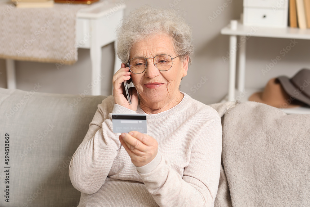 Senior woman with credit card talking by mobile phone on sofa at home Senior woman with credit card talking by mobile phone on sofa at home