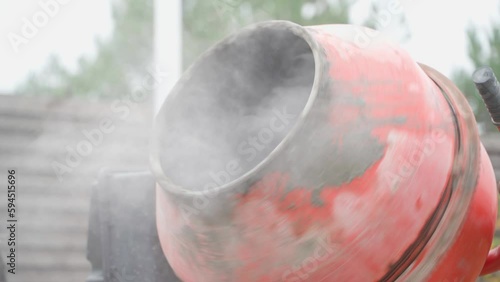 A man pours a plasticizer from a bucket into a working crown mixer, close-up photo