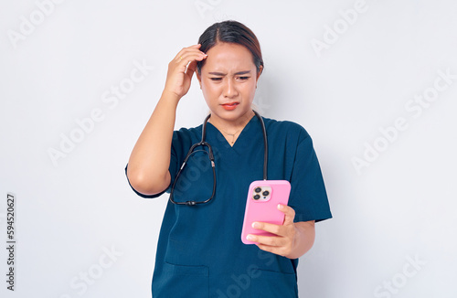 Confused young Asian woman nurse working wearing a blue uniform looking at smartphone screen and emotionally reacting to online news isolated on white background. Healthcare medicine concept
