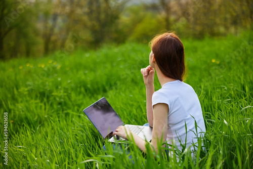 woman working on a laptop while sitting in tall grass in nature photo