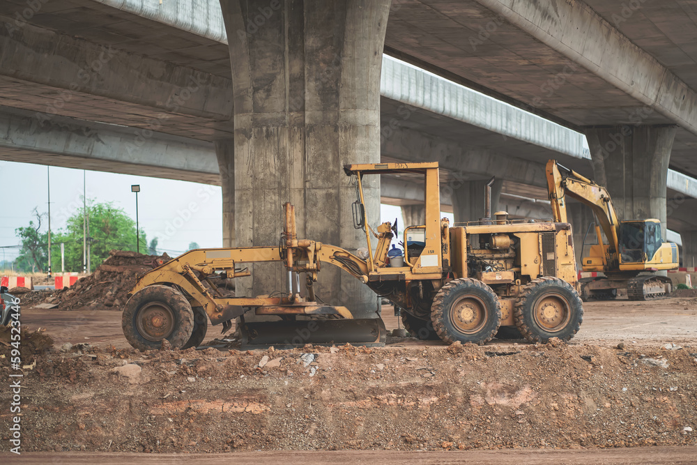 Obraz premium Grader tractor parked in highway construction area near concrete high bridge