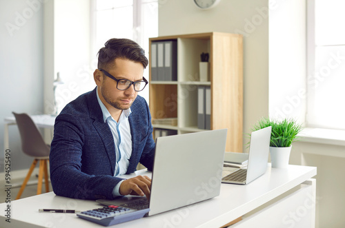Foto Serious busy businessman working on laptop and using calculator for calculations