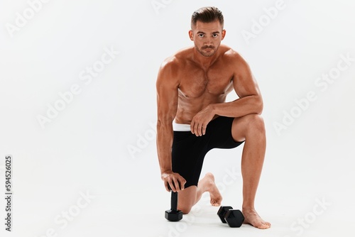 Man athletic body bodybuilder posing with dumbbells with naked torso abs full-length in the background  fitness class. Advertising  sports  active lifestyle  competition  challenge concept. 