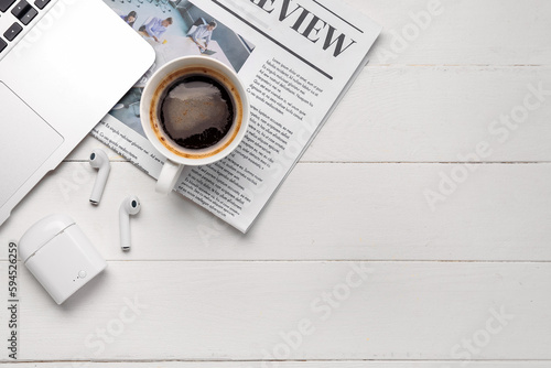 Cup of coffee with earphones  newspaper and laptop on white wooden background