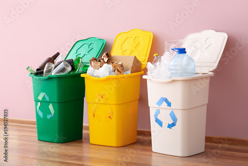 Trash bins with recycling symbol and different garbage near pink wall