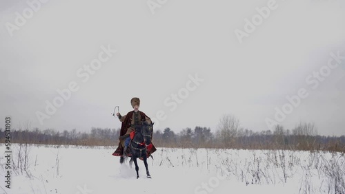 portrait of medieval warrior or messenger riding horse in winter on snowed field, slow motion photo
