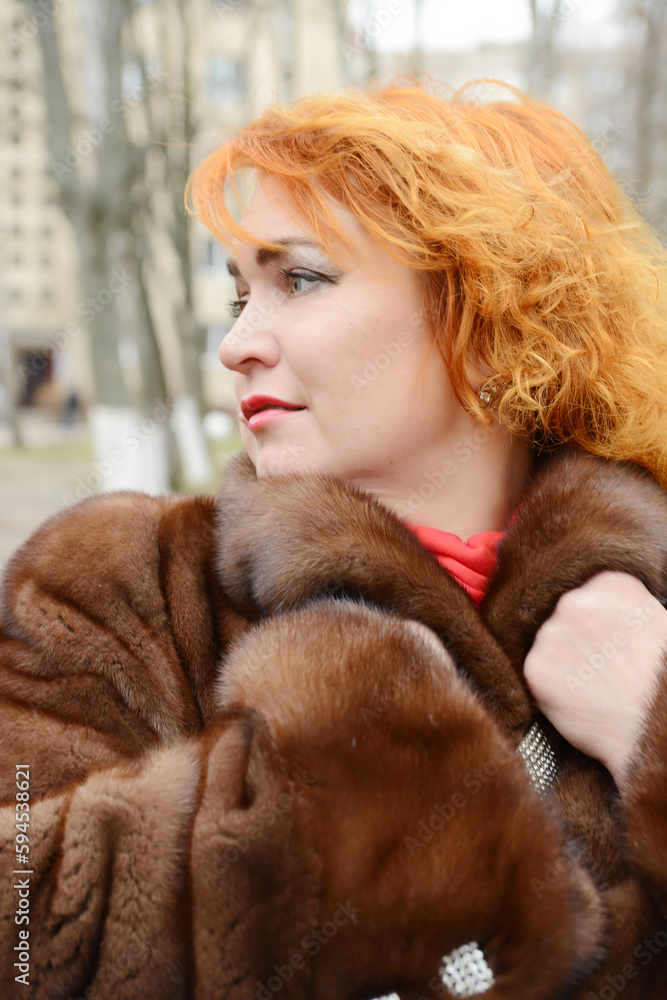 red-haired woman wearing white knitted hat and dressed in warm hooded casual parka jacket outerwear, girl in the parking lot, pedestrian crossing and car in the background, girl warms frozen red-haired woman wearing white knitted hat and dressed in warm hooded casual parka jacket outerwear, girl in the parking lot, pedestrian crossing and car in the background, girl warms frozen
