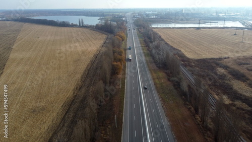 Landscape Highway, driving cars, agricultural fields after harvest, lakes on autumn day. Flying over automobile asphalt road with white markings and many cars. Perspective scenery. Aerial drone view