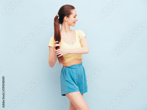 Fototapeta Naklejka Na Ścianę i Meble -  Image portrait of optimistic woman in yellow  t-shirt and blue shorts. Carefree stylish model with hair in ponytail. Smiling female posing in studio. Isolated. Looks delightful and cute. Slim
