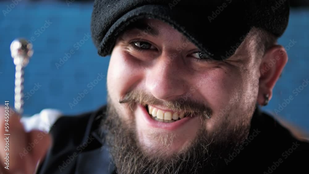 Close up face of authentic professional smiling bearded caucasian bartender with tattoo and hat creating a cocktail drink. Experienced barman mixes a cocktail in glass in bar, drink cocktails concept. Close up face of authentic professional smiling bearded caucasian bartender with tattoo and hat creating a cocktail drink. Experienced barman mixes a cocktail in glass in bar, drink cocktails concept.