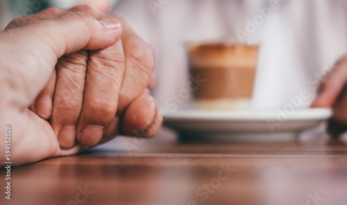 Two old senior people holding hands expressing support and friendship, help and care. Elderly man and woman sitting at cafe table