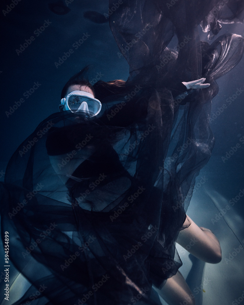 A girl in a mask underwater in the pool in the water