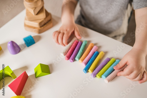 A three-year-old boy plays with crayons, plasticine and a construction set. The concept of early development and sensory perception. Finger games in kindergarten