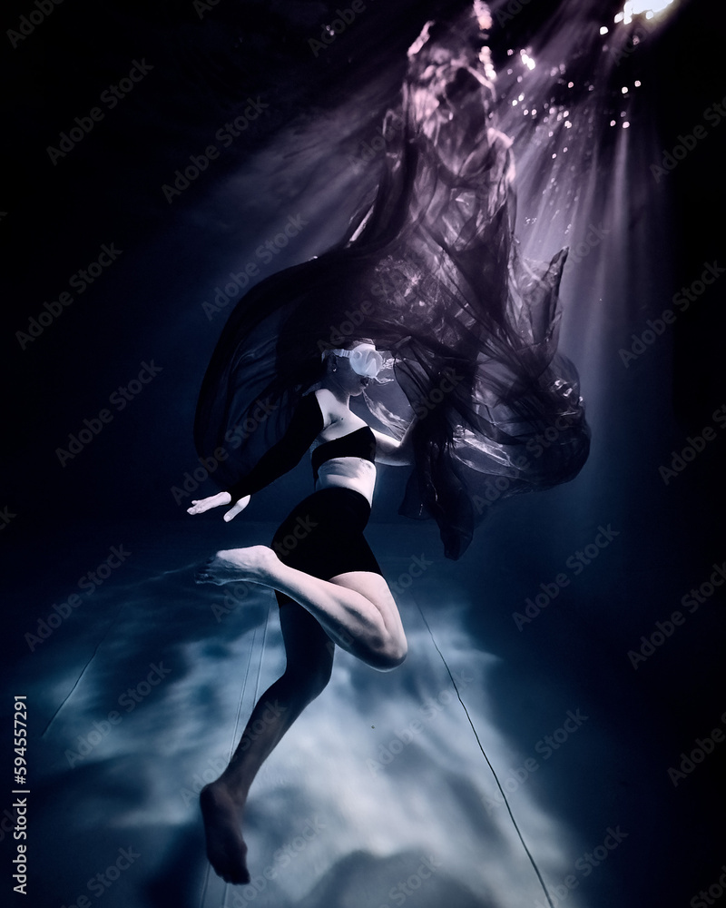 A masked freediver girl dives in a pool underwater with a black fashion fabric