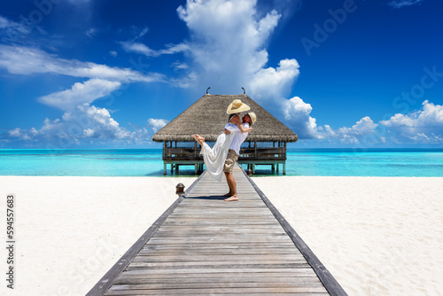 A happy couple in white summer clothing hugging on a wooden pier towards a tropical paradise island in the Maldives, Indian Ocean photo