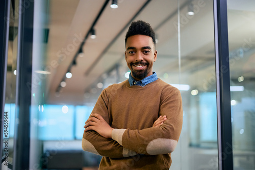 Happy black entrepreneur with arms crossed in office looking at camera.