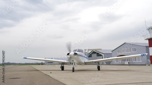 Single engine propeller airplane is standing in front of a closed aircraft hangar. Transportation for tourists and locals. Small white airplane existing hangar preparing for flight. 