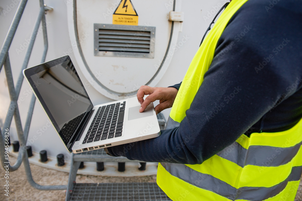 Maintenance electrical engineer checks a wind turbine with a protective vest with a laptop
Maintenance electrical engineer checks a wind turbine with a protective vest with a laptop