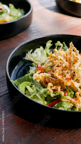deep fried enoki mushroom or golden needle mushroom on top of green salad on black plate, vegan style 