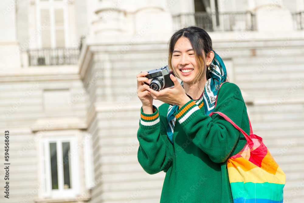 Asian youth with Pride bag and camera, smiling.
