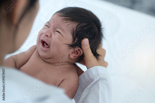 Mother holds 1 month baby girl in arms, baby was feeling sick and crying while mother was holding and comforting her baby, child care concept, Mother's Day photo