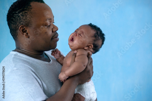 African father holds 3 months old baby girl in arms, baby was feeling sick and crying while father was holding and comforting her baby, child care concept, Father's Day