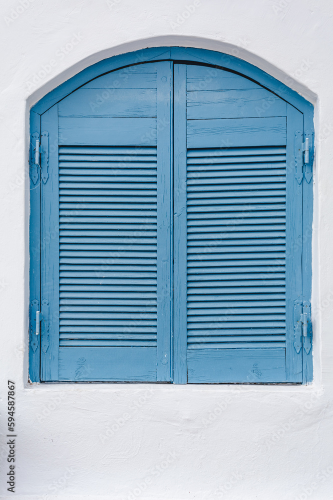 Closed blue wooden shutters on a white painted house facade in mediterranean architectural style Closed blue wooden shutters on a white painted house facade in mediterranean architectural style