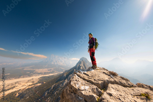 young girl climber in a helmet and with a backpack stands on top of a mountain. mountain climbing