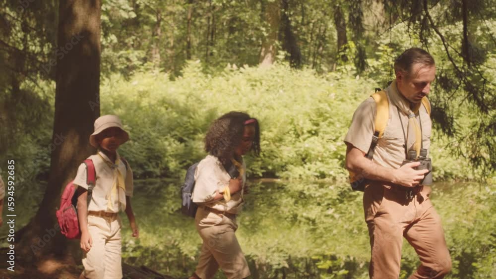 Diverse children in scout uniform following their leader while hiking in summer forest together Diverse children in scout uniform following their leader while hiking in summer forest together