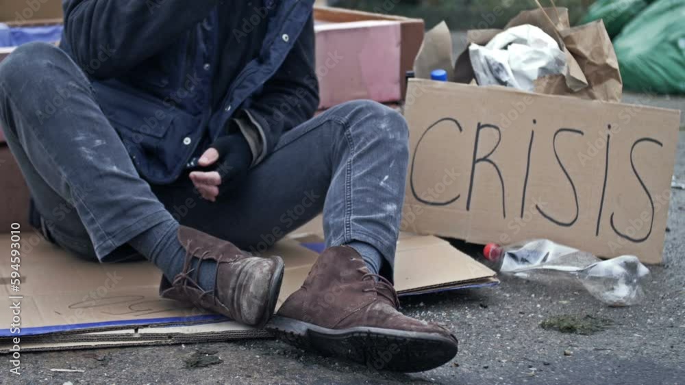 Homeless man, shivering from the cold, sits on a cardboard box among ...
