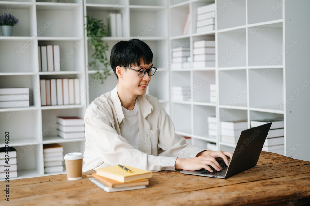 Handsome and talented young Asian man student working on his project assignment, using laptop and tablet to search an online informations.. Handsome and talented young Asian man student working on his project assignment, using laptop and tablet to search an online informations..