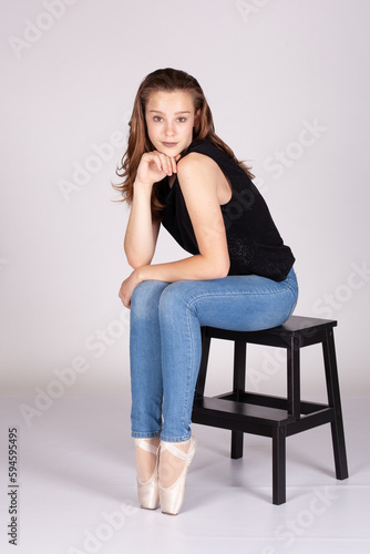 En Pointe resting on stool legs together coy expression looking at the camera hand to chin in a shrug en pointe Beautiful teen girl looking quizically with machiavellian tendencies Metaphor for teens