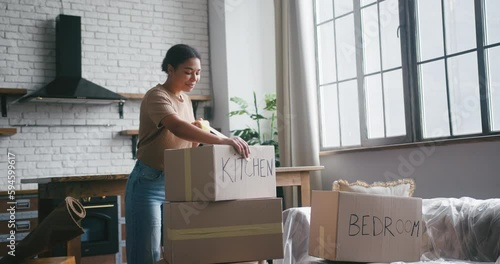 Hispanic woman prepares cardboard boxes for moving in flat