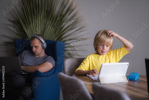 Schoolboy studying at home with digital tablet and doing school homework by himself, Distance learning online education, Training books and notebooks on table