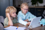 Online school class, siblings pupils boy and girl learning together remotely online at home, looking to digital tablet, speaking with teacher or tutor using internet