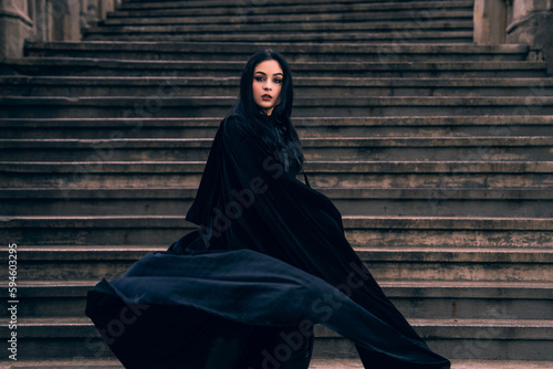 a woman in a black dress standing on a set of stairs with her hands in her pockets and her eyes closed, a matte painting, gothic art