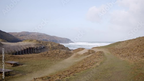 Static shot of a woman walking towards a beach across the machair (sea grass). Cliffs and headland are visible. Filmed on the Isle of Lewis, part of the Outer Hebrides of Scotland. photo