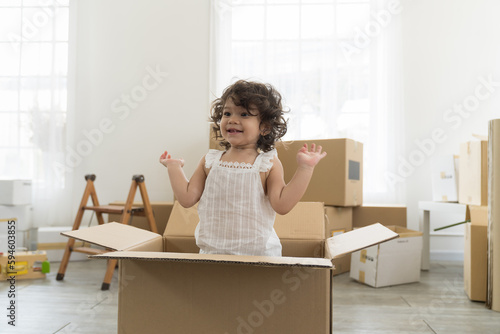 Moving house, mortgage, family and real estate concept. Happy cute little daughter baby toddler girl playing inside of cardboard box family moving into new house photo