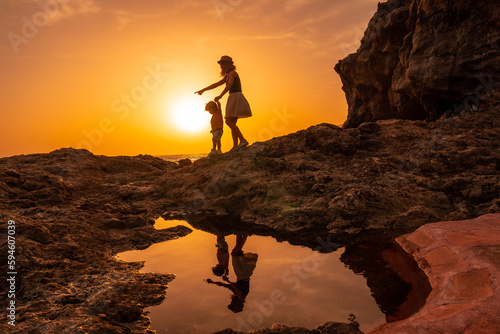 Silhouette of mother and son walking in the sunset on the beach of Tacoron in El Hierro  Canary Islands  vacation concept  orange sunset  walking by the sea pointing the path