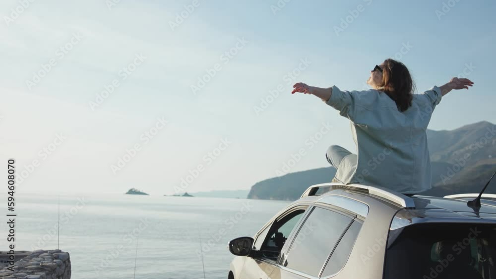 A young Caucasian woman sitting on the roof of her car parked by the sea and enjoying the beautiful view. A young Caucasian woman sitting on the roof of her car parked by the sea and enjoying the beautiful view.