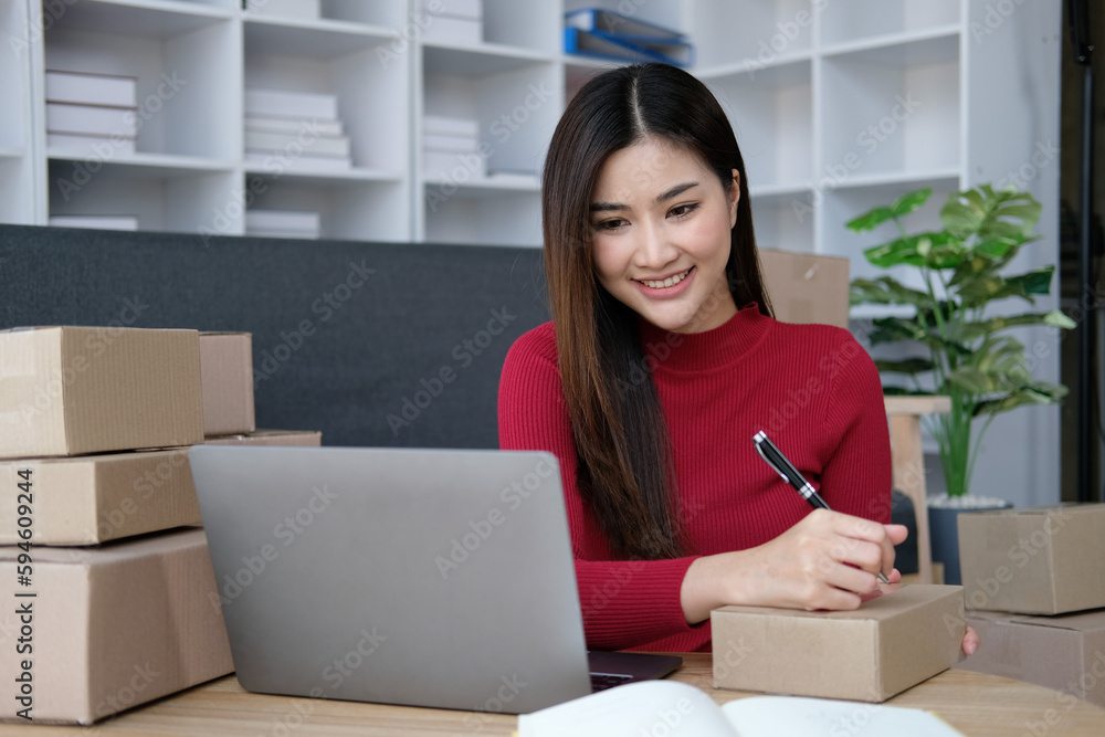 Young Asian woman working from home with laptop and boxes checking orders and preparing parcel delivery, SME online business concept Young Asian woman working from home with laptop and boxes checking orders and preparing parcel delivery, SME online business concept