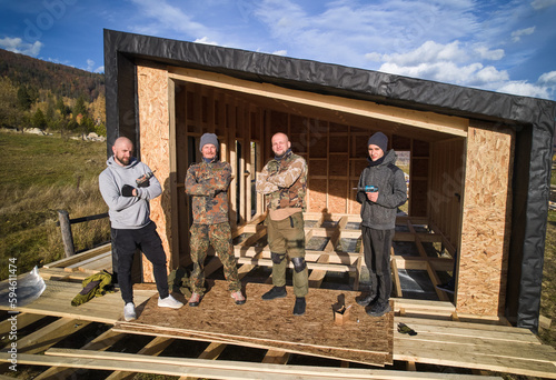 Fotografie Male builders standing on terrace of unfinished wodden house in Scandinavian style barnhouse