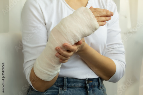 Close-up of a woman's broken arm in plaster bandage. Injured caucasian woman in a white t-shirt standing and holding her wrist in a plaster cast with physical pain in a fractured bone.