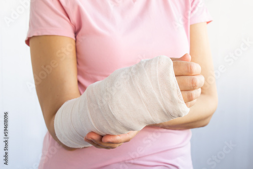 Close-up of a broken arm of a woman in a cast in a pink t-shirt on a white background. Accident insurance. Traumatology and insurance medicine.