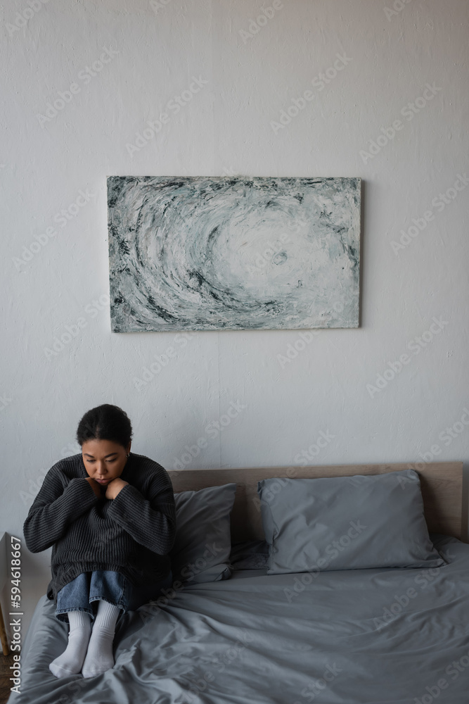 Young multiracial woman with depression sitting on bed at home.