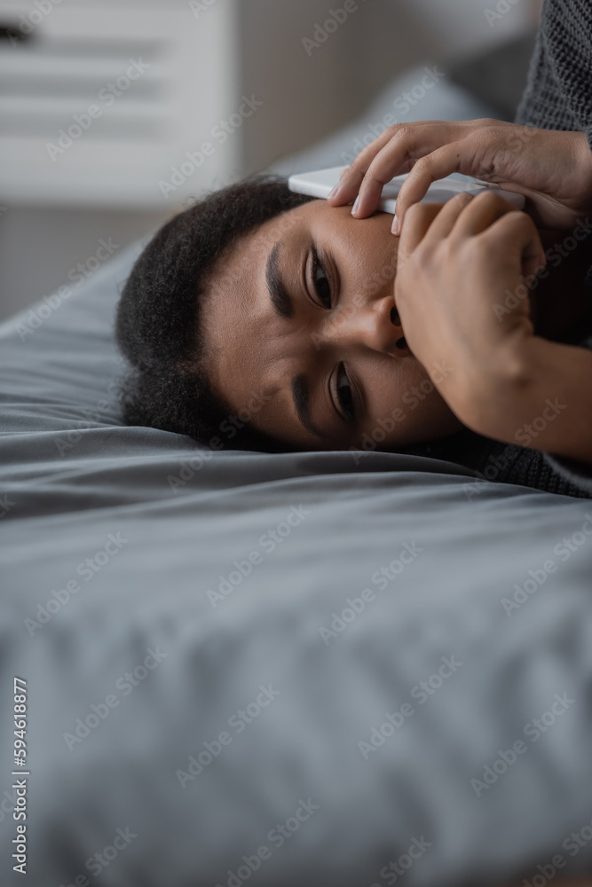 Upset multiracial woman talking on smartphone while lying on bed at home. Upset multiracial woman talking on smartphone while lying on bed at home.